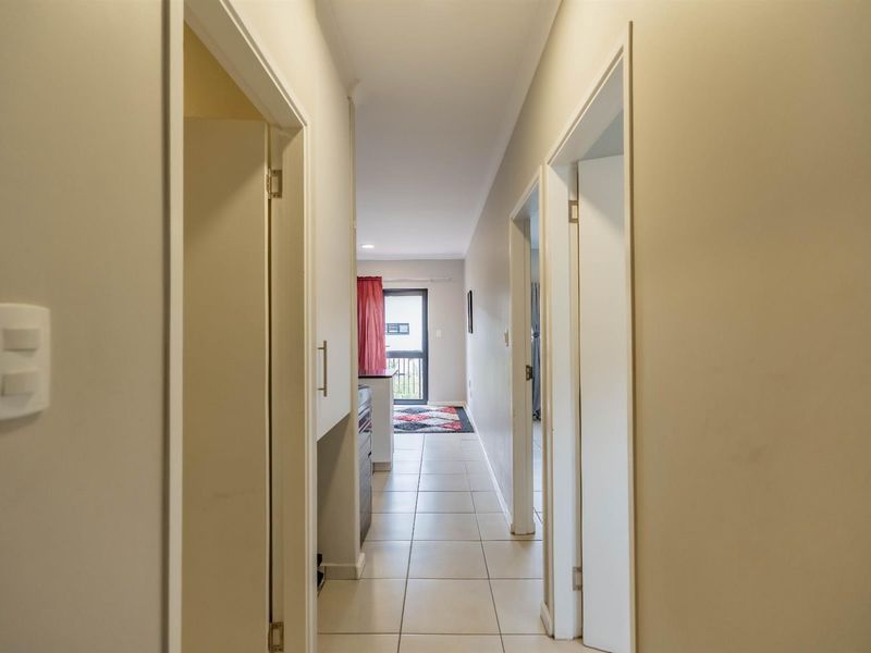 A clean, neutral-toned hallway with tiled flooring, providing access to adjacent rooms and leading towards an exterior door.