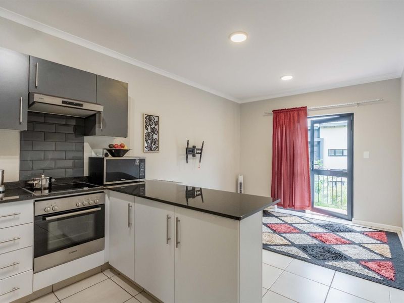 Modern open-plan kitchen featuring sleek cabinetry, granite countertops, and integrated appliances, flowing seamlessly into a living area with direct access to a balcony.