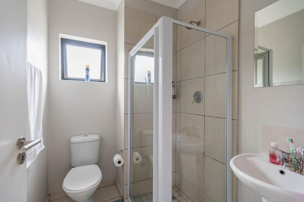 Compact bathroom featuring a shower enclosure, white toilet, and wall-mounted basin with neutral wall tiling.