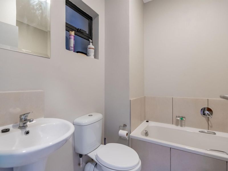 A clean and functional bathroom featuring a pedestal washbasin, a standard toilet, and a bathtub with tiled splashback.