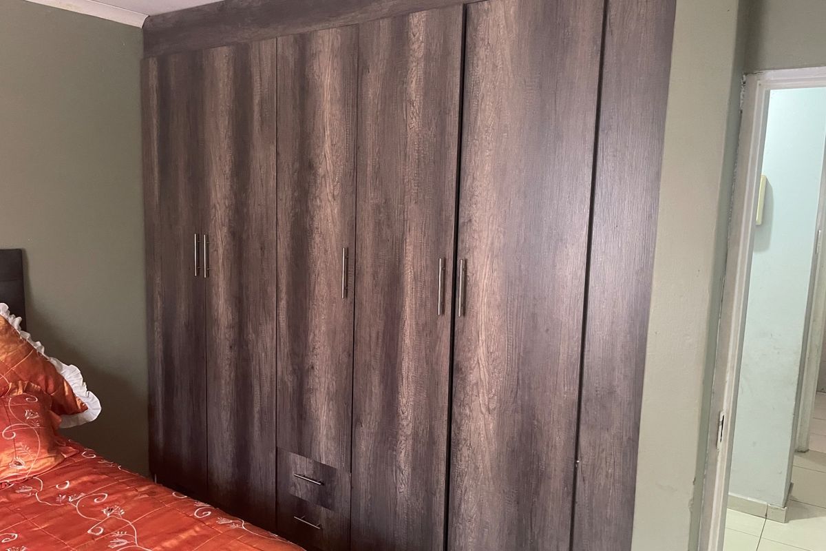 A bedroom featuring floor-to-ceiling dark wood-grain built-in cupboards with integrated drawers and modern metal handles.