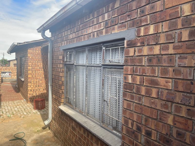 Exterior view of the rear brick facade featuring steel-framed windows with security bars and functional guttering system.