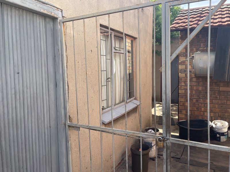 Rear exterior view showing a metal security gate, brick walling, and a window with visible wear and maintenance requirements.
