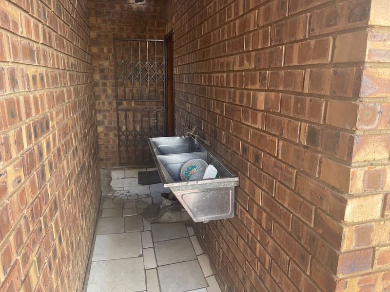 A functional outdoor laundry area featuring a stainless steel double sink, exposed brick walls, and tiled flooring.