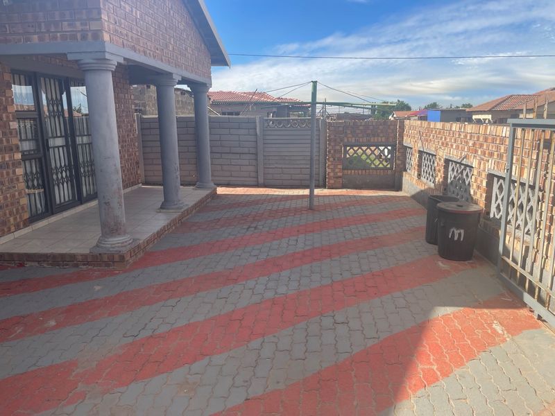 A paved outdoor patio area featuring brick construction, decorative columns, and a secure perimeter wall, providing a functional space for outdoor activities.