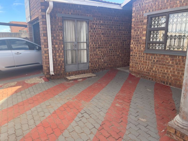 Front exterior view of a face brick house featuring a paved driveway with security gates and window bars.