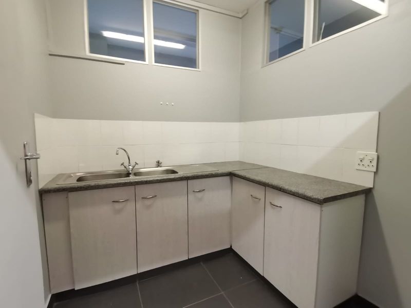 A clean and functional scullery or kitchenette area featuring built-in cabinetry, a stainless steel sink, stone countertops, and tiled backsplash.