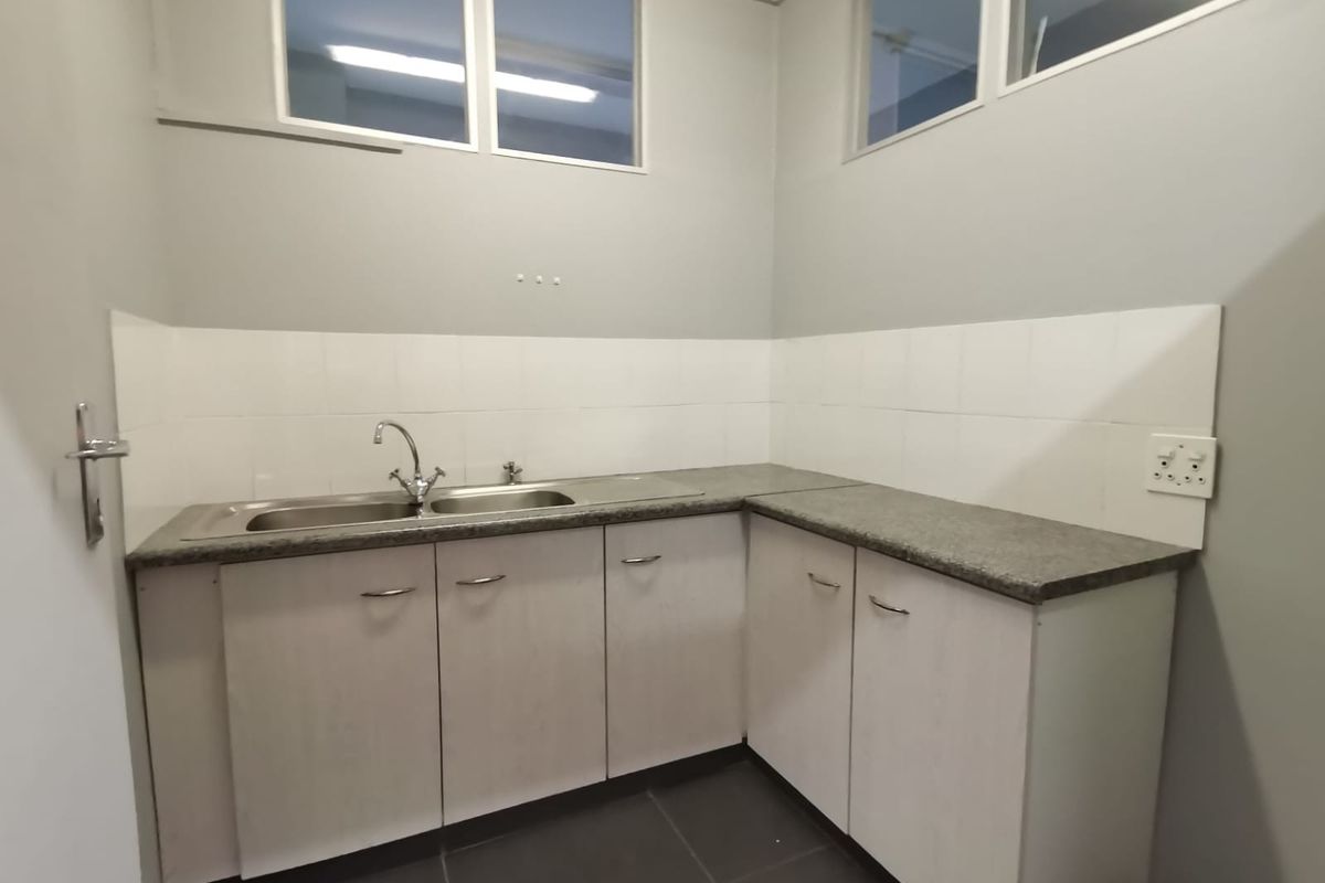 A clean and functional scullery or kitchenette area featuring built-in cabinetry, a stainless steel sink, stone countertops, and tiled backsplash.