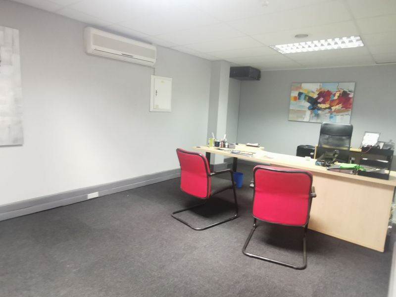 A functional office space featuring a suspended ceiling, recessed lighting, carpeted flooring, and a wall-mounted split-system air conditioning unit.