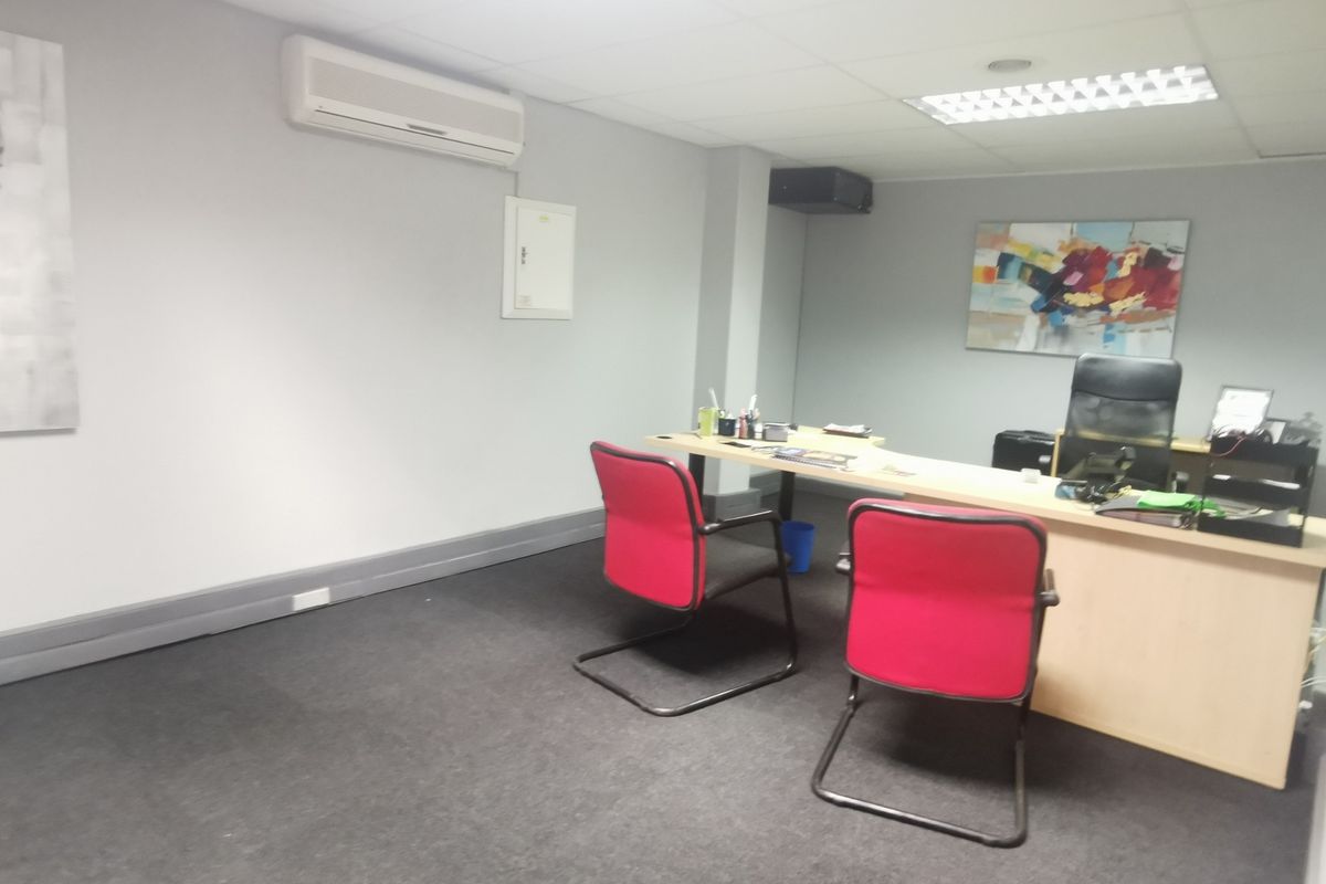 A functional office space featuring a suspended ceiling, recessed lighting, carpeted flooring, and a wall-mounted split-system air conditioning unit.