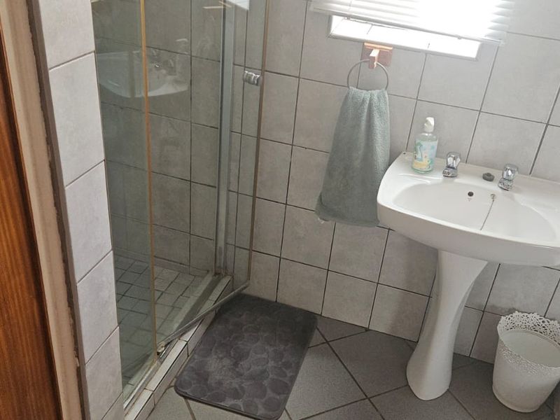 A functional bathroom featuring a pedestal washbasin, a glass-enclosed shower, and a bathtub with tiled wall and floor finishes.