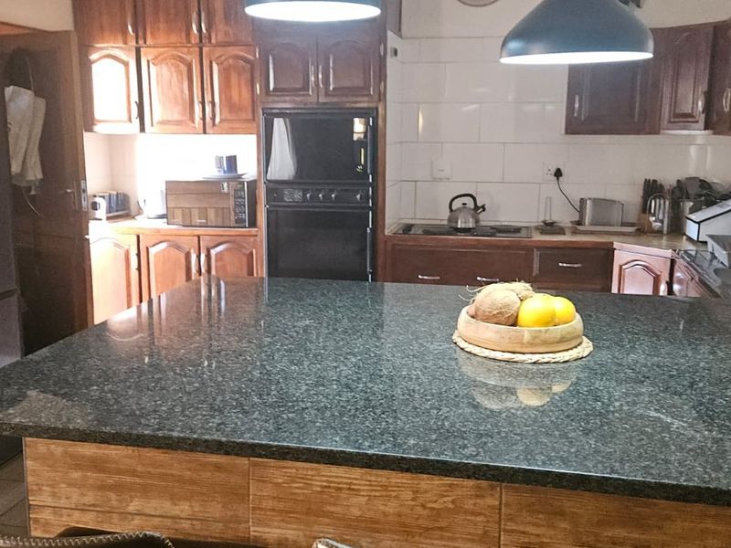 A functional kitchen featuring wooden cabinetry, a large granite-topped island, built-in oven, and a tiled splashback.