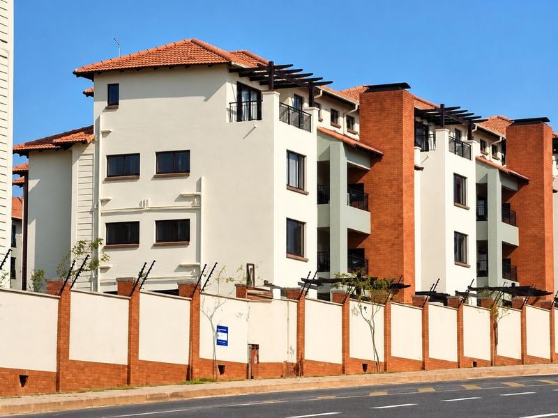 A well-maintained multi-story apartment complex featuring a secure perimeter wall with electric fencing, tiled roofing, and modern architectural brick and plaster finishes.