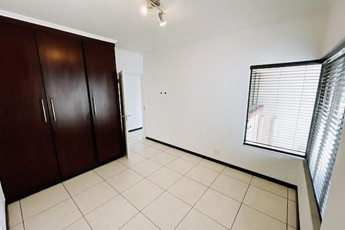 A bright, empty bedroom featuring tiled flooring, built-in dark wood cupboards, and venetian blinds on the windows.