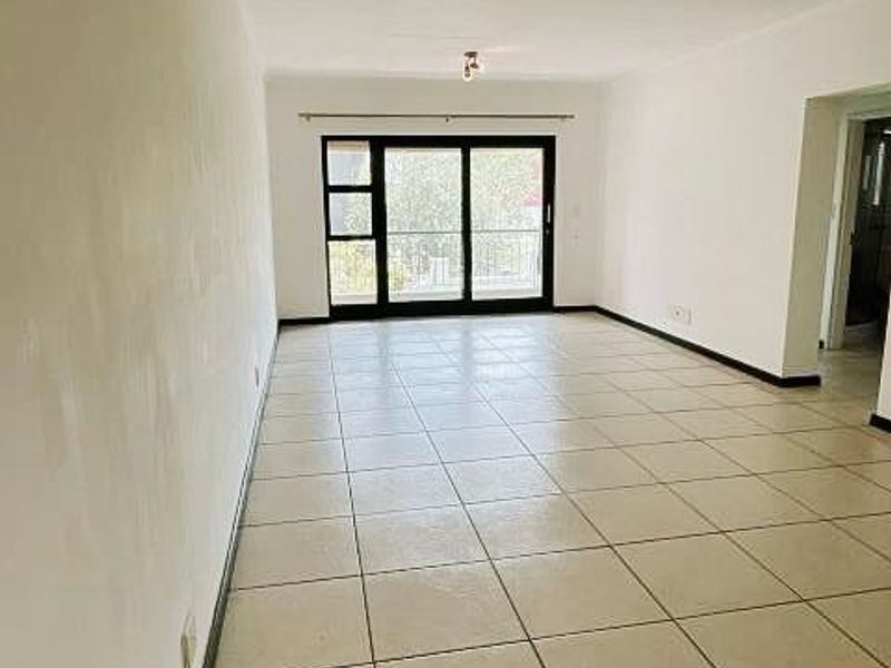 A spacious, empty living area featuring neutral tiled flooring, ceiling spotlights, and a large sliding glass door leading to an outdoor space.
