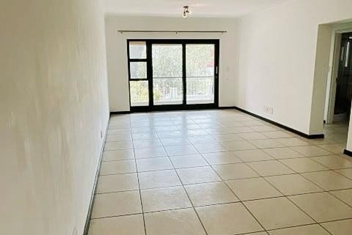 A spacious, empty living area featuring neutral tiled flooring, ceiling spotlights, and a large sliding glass door leading to an outdoor space.