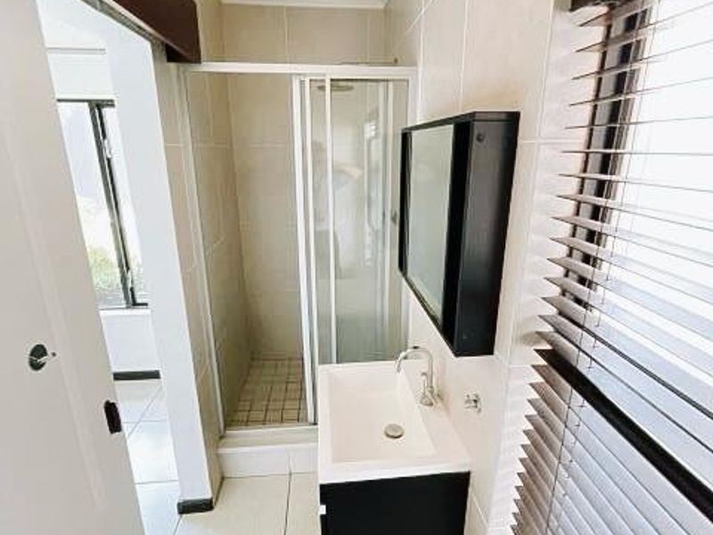 A clean and modern bathroom featuring a glass shower enclosure, wall-mounted vanity with basin, and neutral floor-to-ceiling tiling.