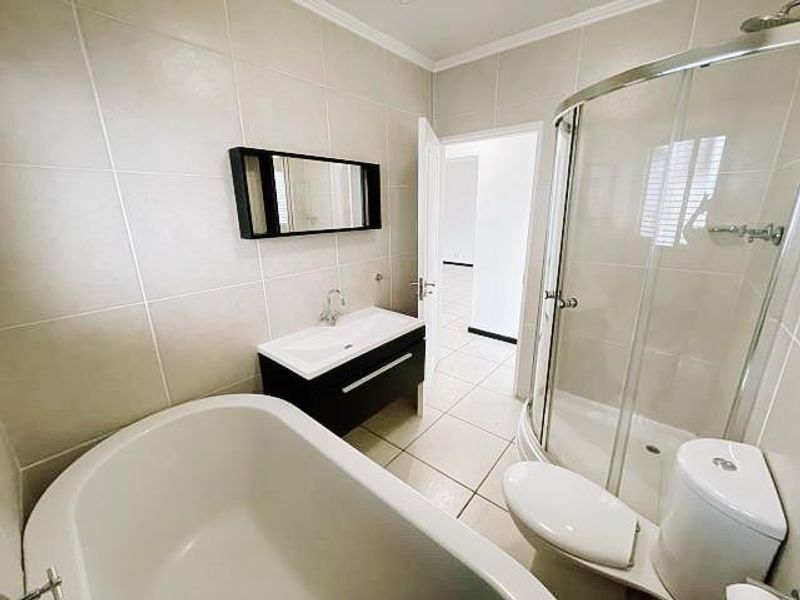 Modern bathroom featuring a freestanding bathtub, a separate curved glass shower enclosure, and a sleek vanity cabinet with a wall-mounted mirror.