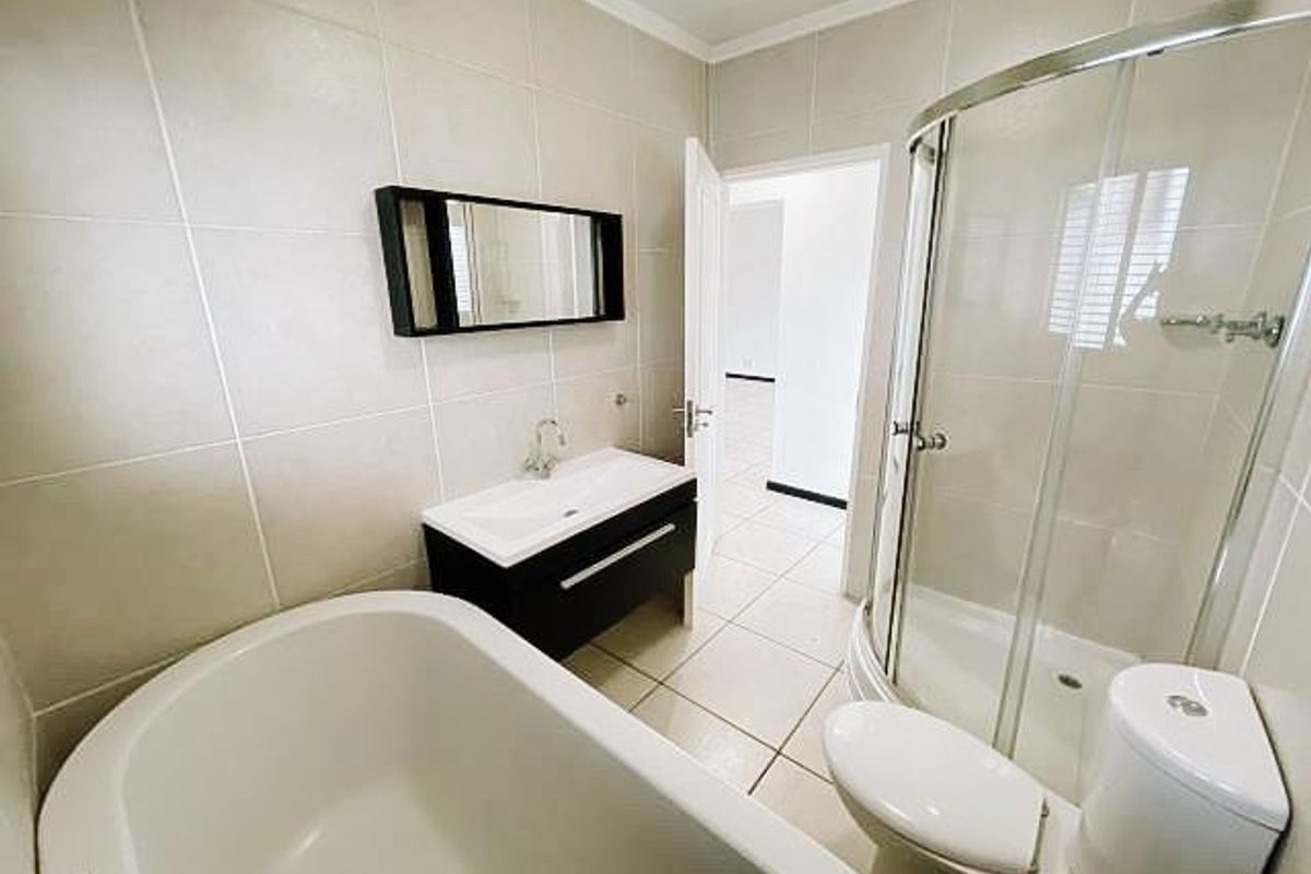 Modern bathroom featuring a freestanding bathtub, a separate curved glass shower enclosure, and a sleek vanity cabinet with a wall-mounted mirror.