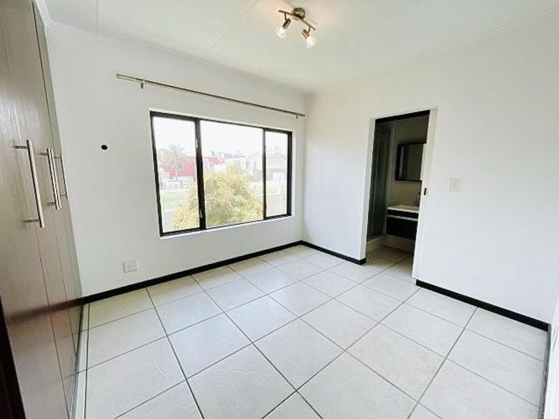 A bright, empty bedroom featuring tiled flooring, built-in cupboards, and direct access to an en-suite bathroom.