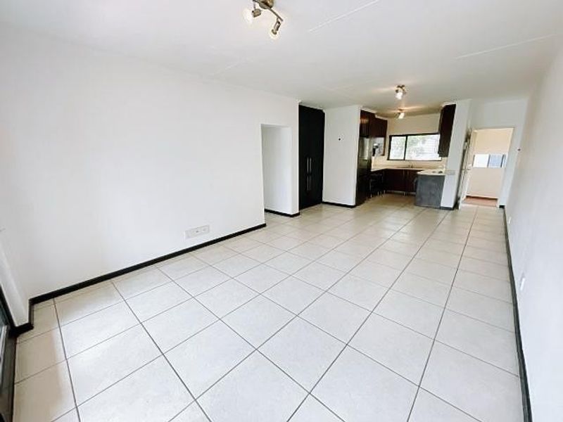 Spacious open-plan living and kitchen area featuring neutral tiled flooring and built-in cabinetry, offering a versatile layout for modern apartment living.