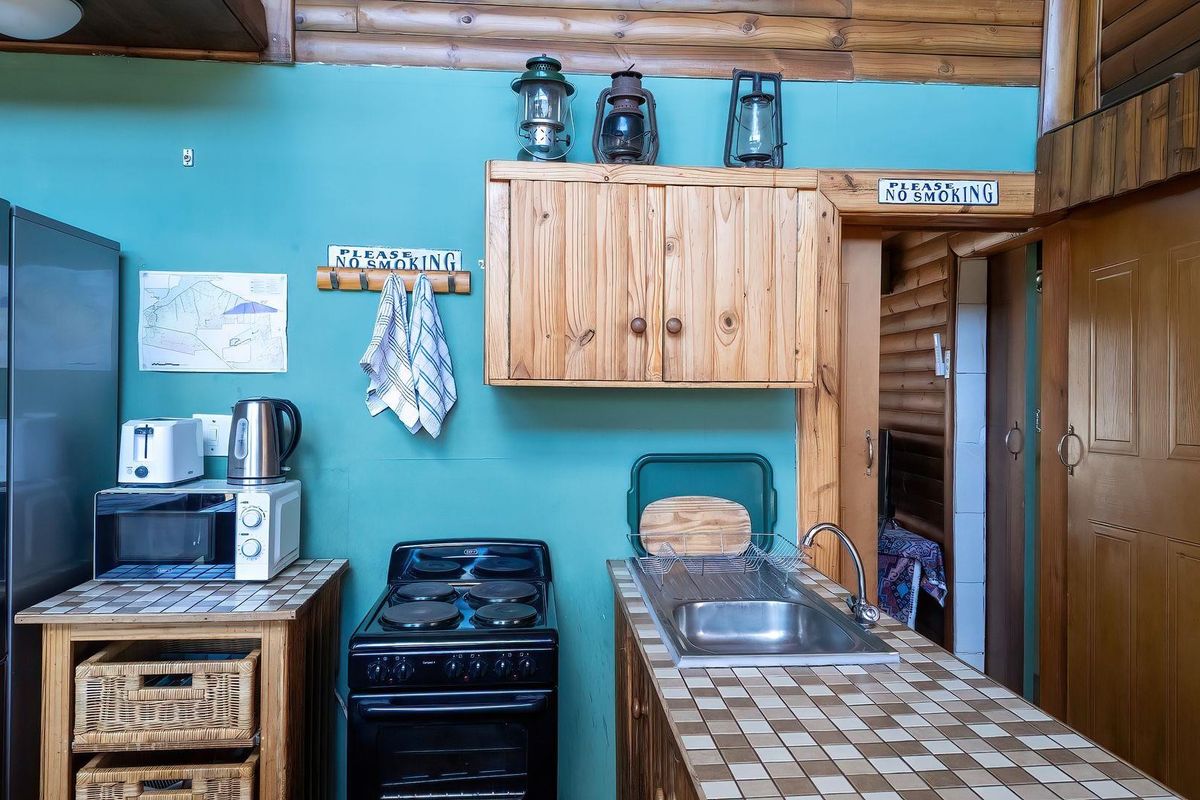 Compact kitchen area featuring a tiled countertop, stainless steel sink, electric stove, and rustic timber wall paneling in a farm-style setting.