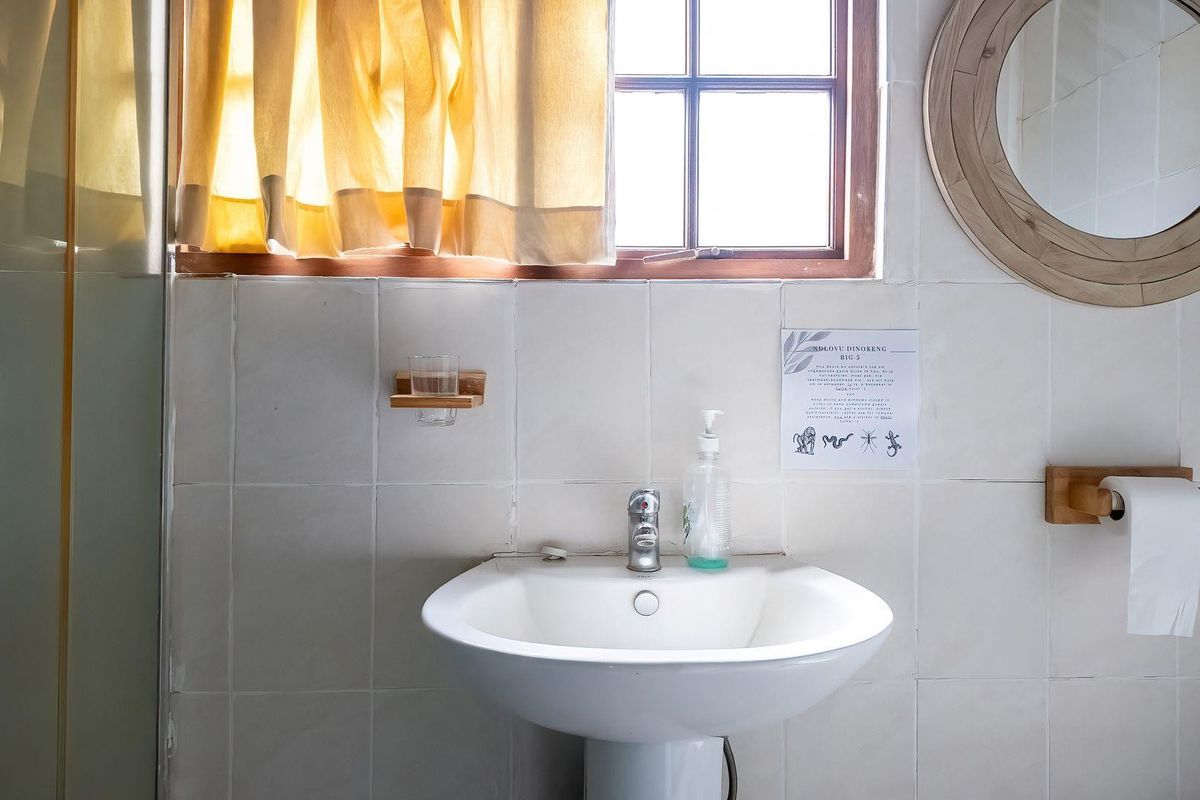 A functional bathroom featuring a pedestal basin, chrome mixer tap, and tiled walls with a timber-framed window providing natural light.