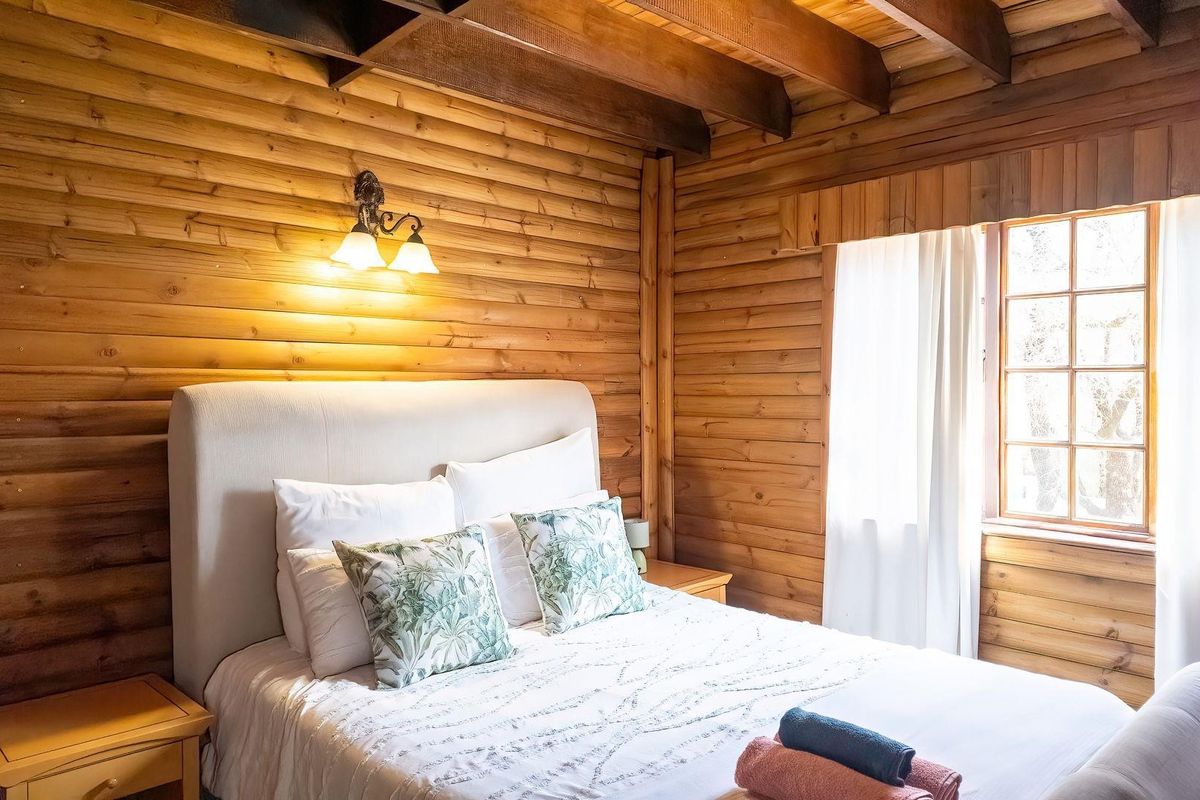A cozy bedroom featuring rustic timber log walls and exposed ceiling beams, creating a warm and inviting atmosphere with natural light.