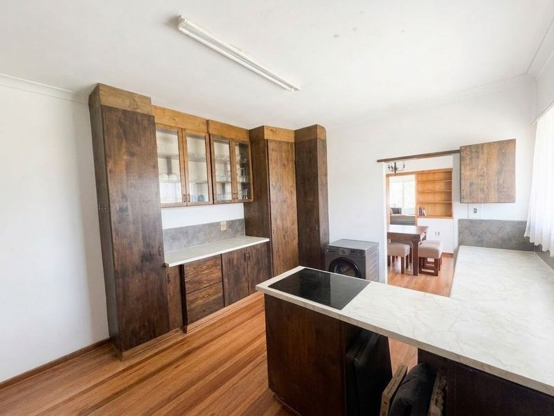 A functional kitchen featuring dark wood cabinetry, laminate countertops, an integrated electric cooktop, and warm hardwood flooring, with an open flow to the dining area.