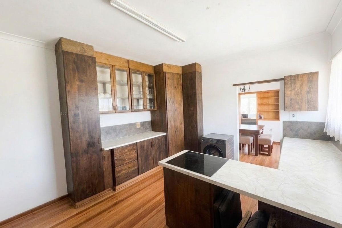 A functional kitchen featuring dark wood cabinetry, laminate countertops, an integrated electric cooktop, and warm hardwood flooring, with an open flow to the dining area.