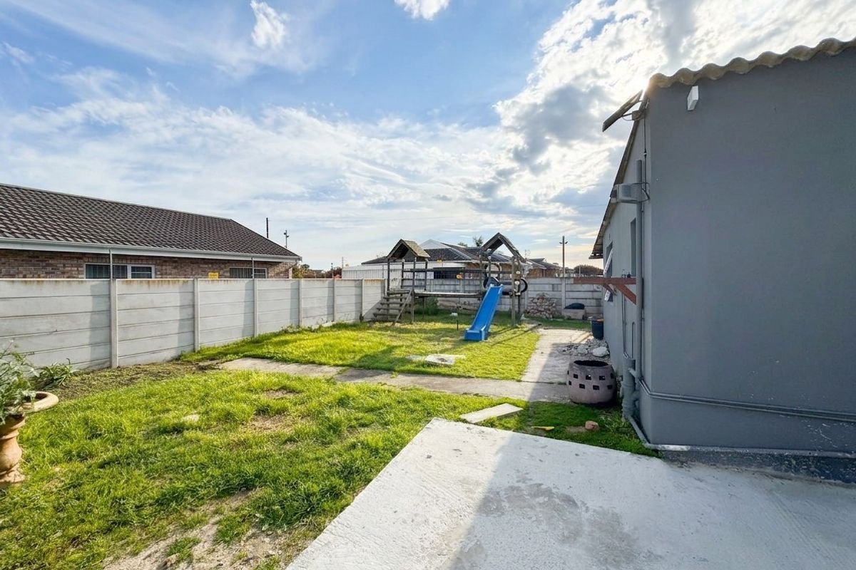 Rear garden area featuring a concrete patio, lawn, and precast concrete boundary walling.