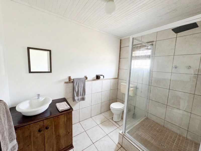 A functional bathroom featuring a vanity with a vessel sink, a glass-enclosed shower, and neutral wall and floor tiling.