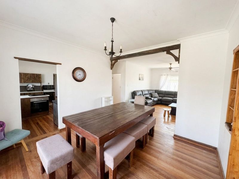 Open-plan living and dining area featuring hardwood flooring, exposed timber beam detailing, and a connected kitchen with built-in cabinetry and appliances.
