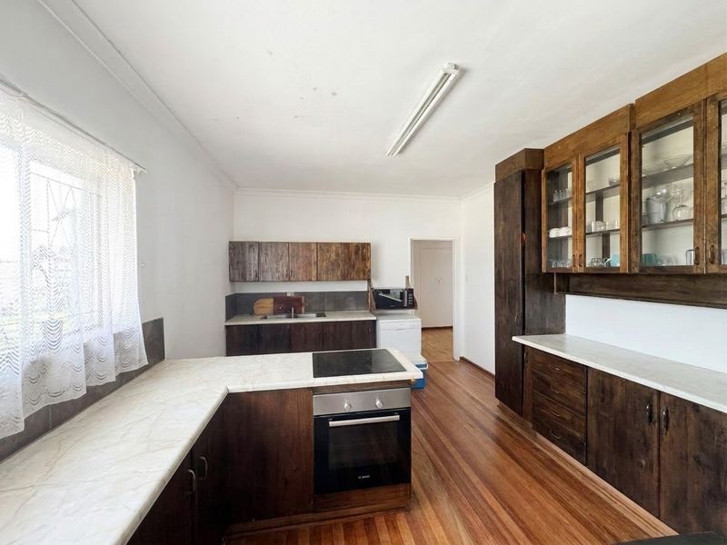 A functional kitchen featuring dark wood cabinetry, laminate countertops, built-in oven, electric hob, and hardwood flooring, offering a classic aesthetic with potential for modernization.