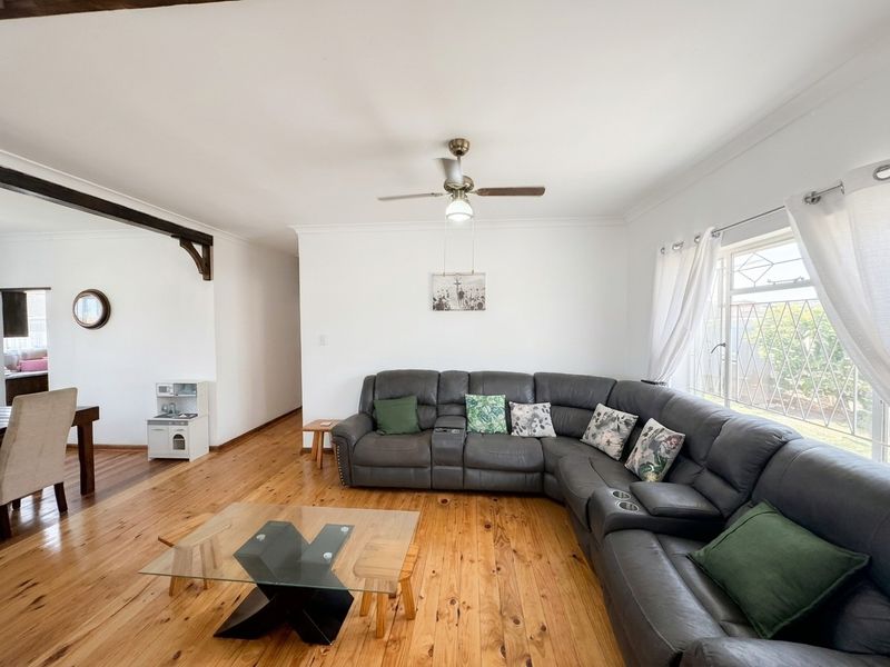 Spacious living room featuring polished hardwood flooring, a ceiling fan, and an exposed timber beam, offering a bright and comfortable atmosphere.