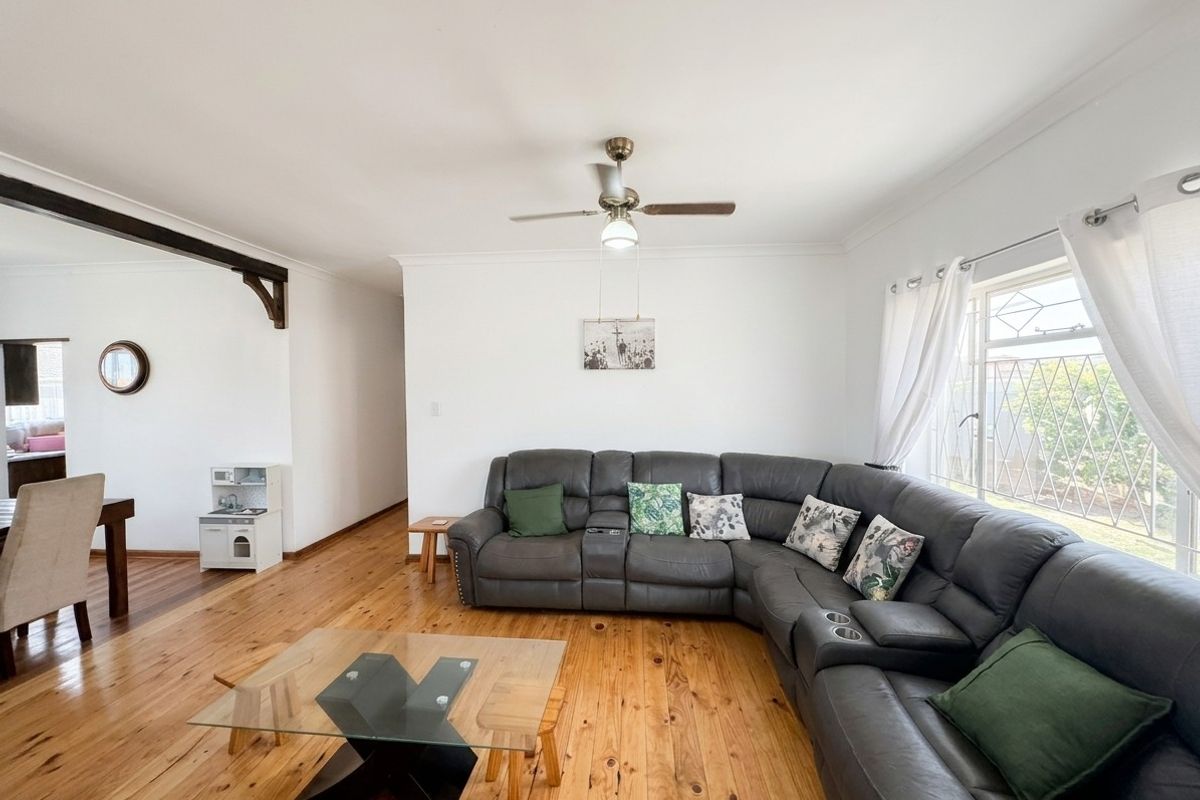 Spacious living room featuring polished hardwood flooring, a ceiling fan, and an exposed timber beam, offering a bright and comfortable atmosphere.
