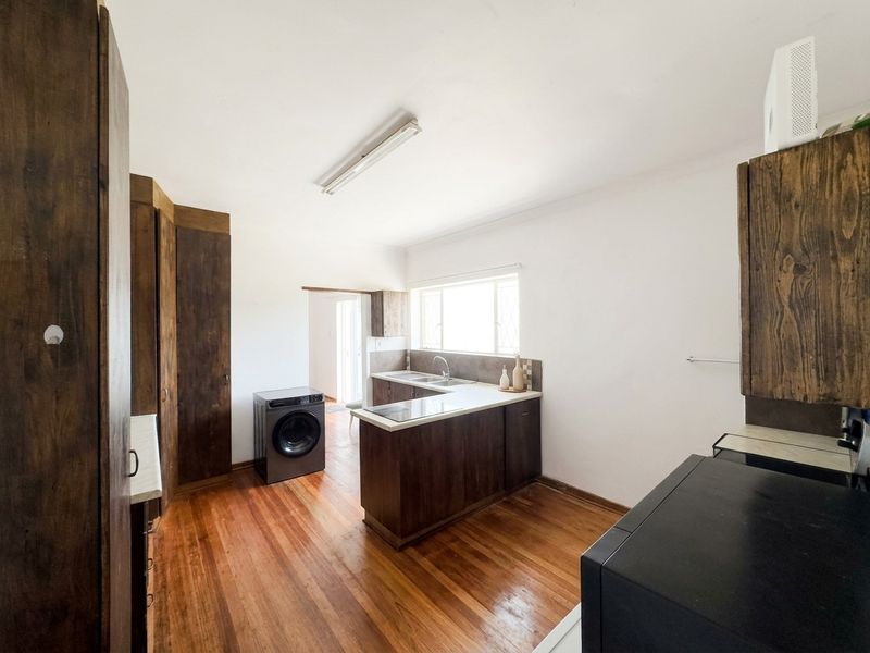A functional kitchen featuring dark wooden cabinetry, laminate countertops, a stainless steel sink, and warm hardwood flooring throughout the space.