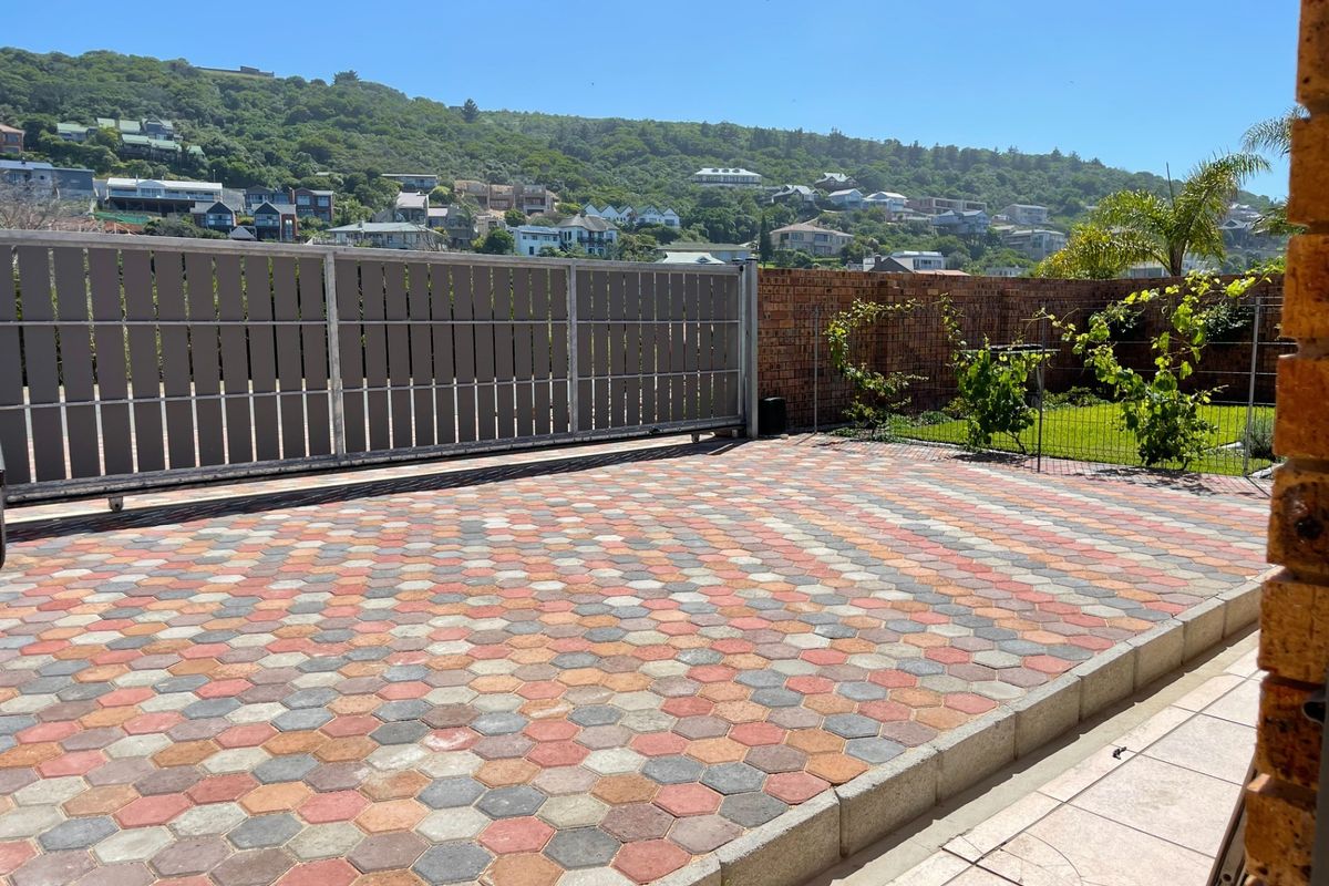 A well-maintained rear exterior area featuring a paved driveway with hexagonal pavers, a secure sliding gate, and a brick boundary wall.