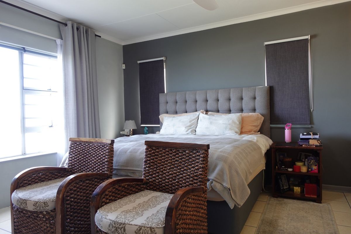 A well-maintained bedroom featuring a dark accent wall, tiled flooring, ceiling fan, and integrated window treatments.