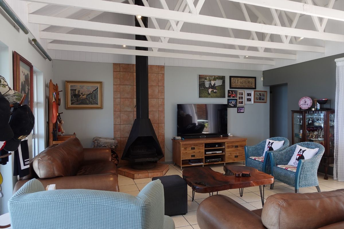 Spacious living room featuring exposed white timber rafters, a central freestanding fireplace with tiled surround, and neutral tiled flooring.