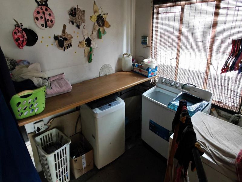 A functional laundry area featuring a built-in timber countertop, plumbing connections for appliances, and window blinds for privacy.