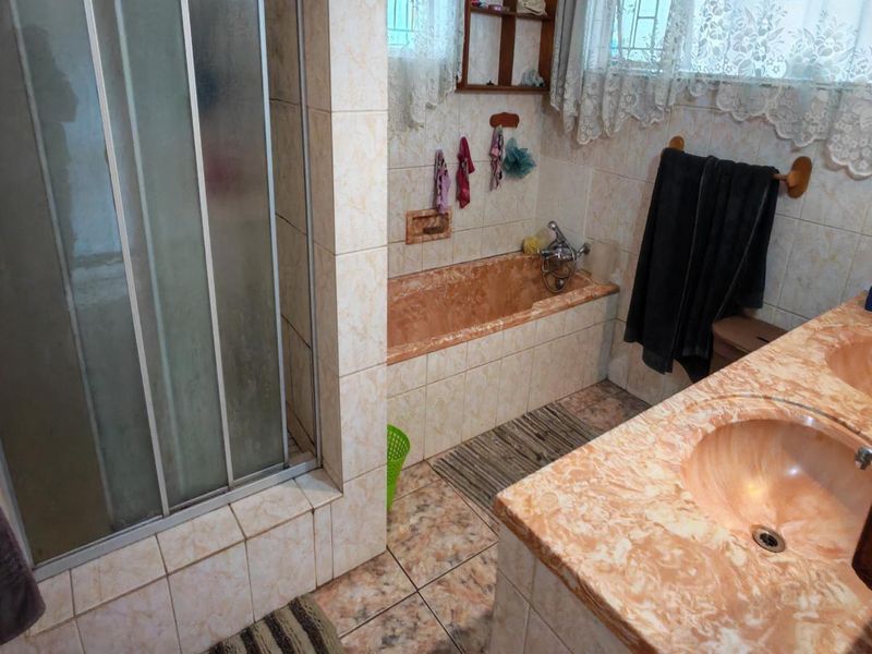 A dated bathroom featuring a shower enclosure, built-in bathtub, and a double vanity with marble-effect countertops and tiled finishes throughout.