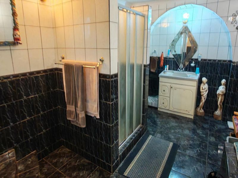 A dated bathroom featuring a shower enclosure, vanity basin, and dark tiled walls with an arched architectural detail.