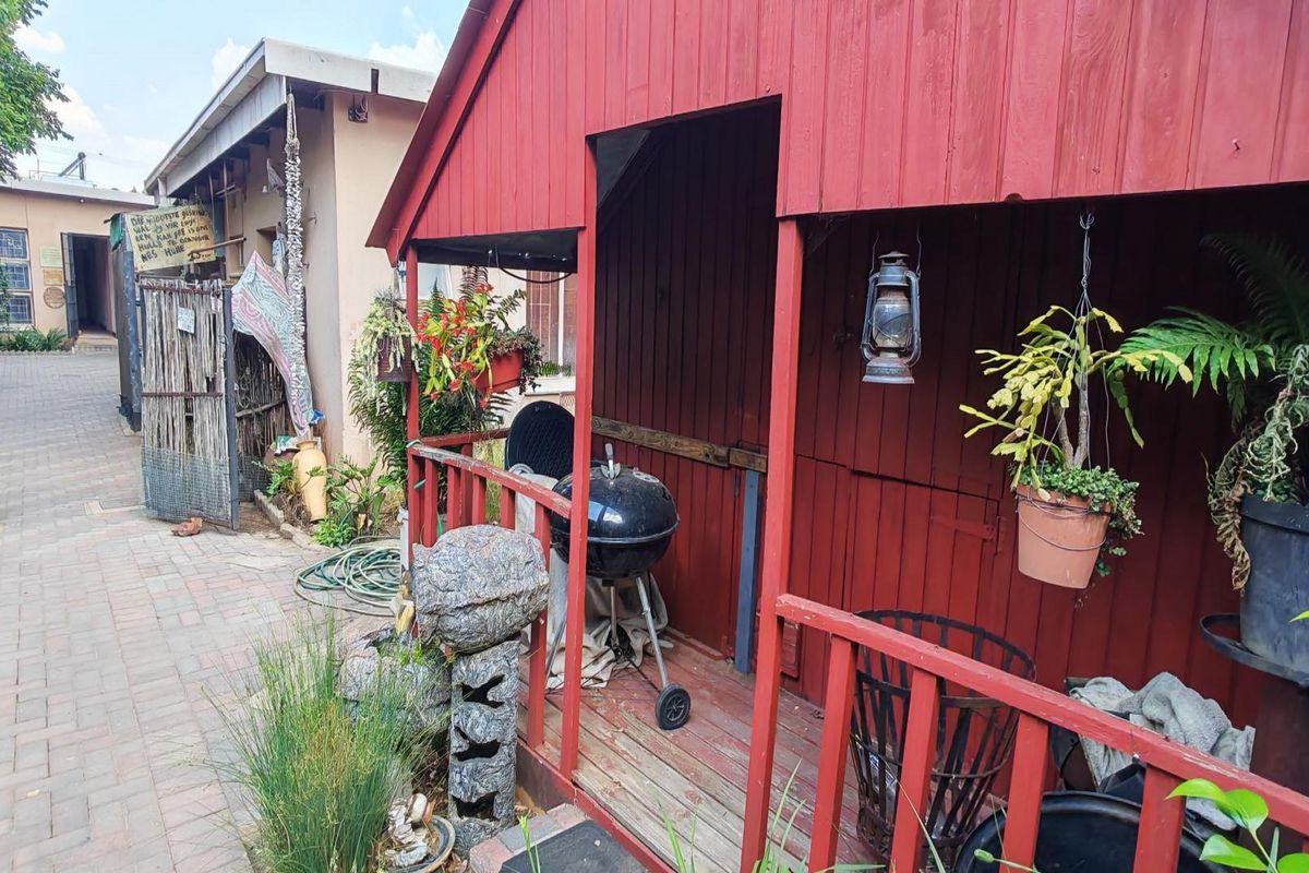 A rustic red timber structure featuring a small covered deck area, suitable for outdoor storage or a garden retreat.