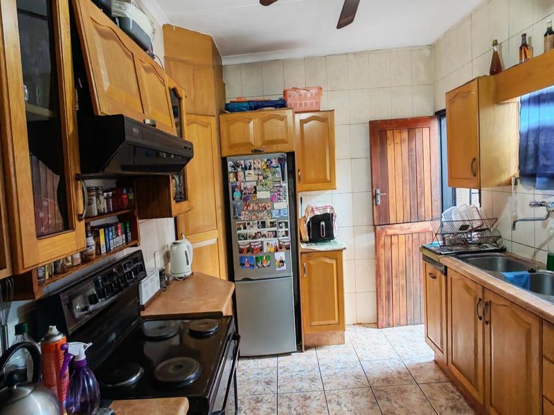 A functional kitchen featuring wooden cabinetry, laminate countertops, an electric stove with extractor fan, and a double bowl sink with tiled splashback.