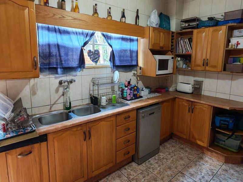 A functional kitchen featuring wooden cabinetry, double basin sink, tiled backsplash, and built-in dishwasher, offering potential for a modern renovation.
