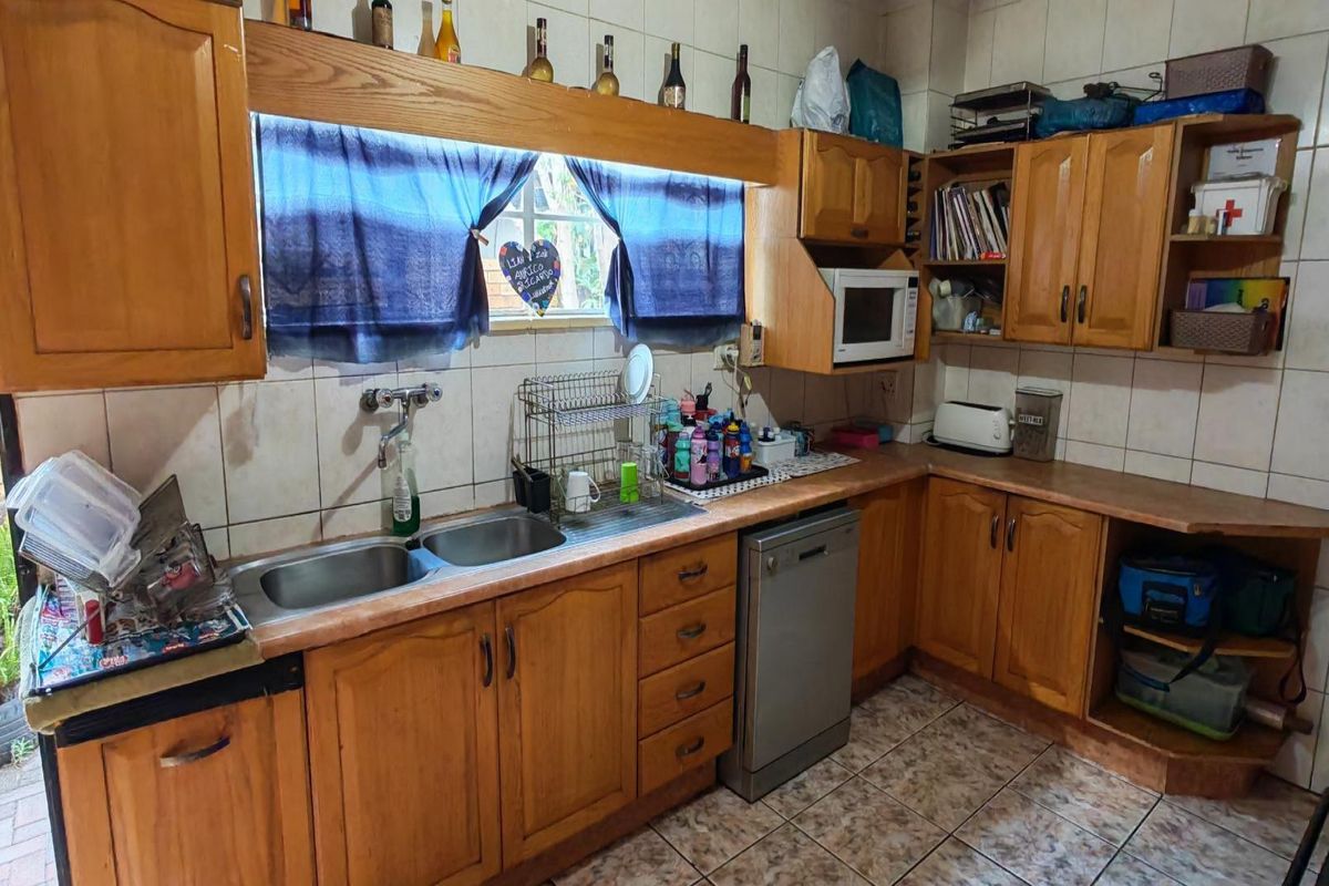 A functional kitchen featuring wooden cabinetry, double basin sink, tiled backsplash, and built-in dishwasher, offering potential for a modern renovation.