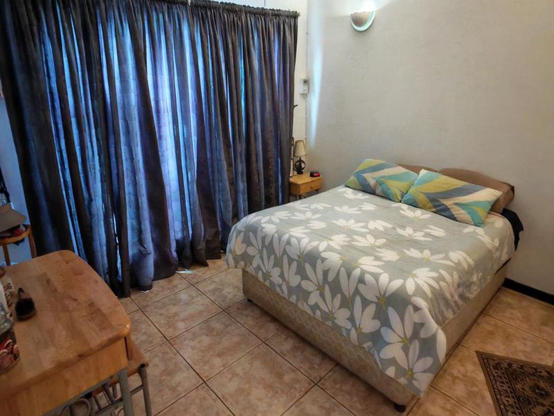 A functional bedroom featuring tiled flooring and a wall-mounted light fixture, providing a neutral base for potential interior updates.