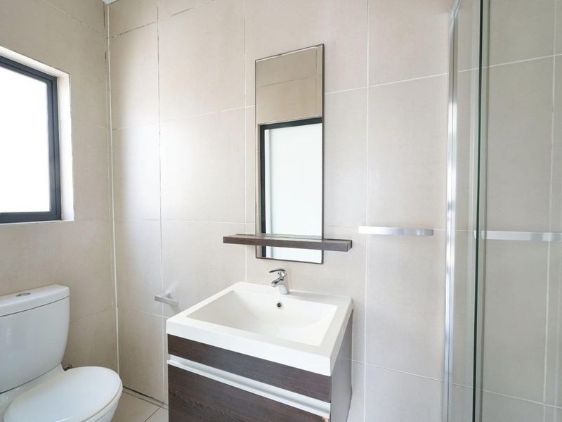 A clean, modern bathroom featuring a vanity with basin, a glass-enclosed shower, and neutral wall tiling.