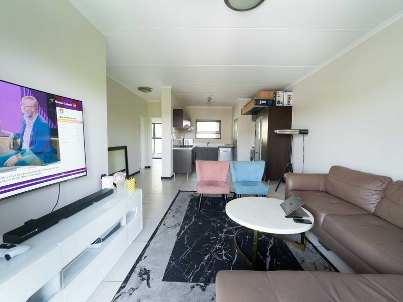 Open plan living area featuring tiled flooring and a connected kitchen space with built-in cabinetry and sink.